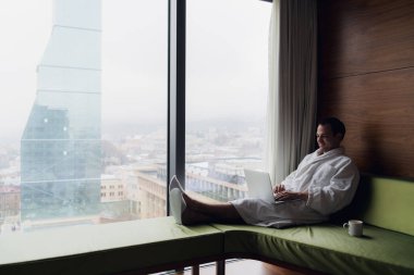 Kahve içme ve dizüstü bilgisayar sabahleyin yatakta kullanarak mutlu adam