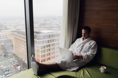 Kahve içme ve dizüstü bilgisayar sabahleyin yatakta kullanarak mutlu adam