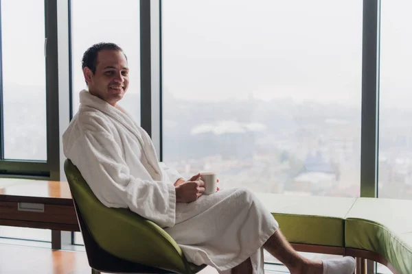 Carefree guy relaxing with hot drink at luxury apartments with great city view