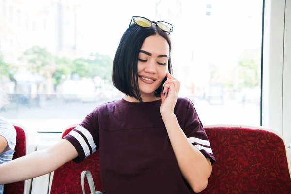 Joven mujer feliz sentada en el autobús de la ciudad y hablando por teléfono móvil . — Foto de Stock