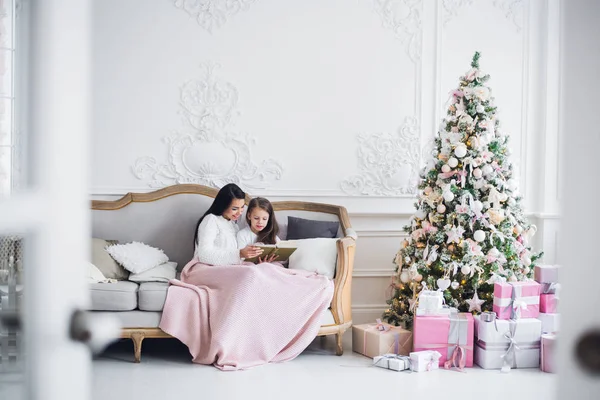 Véspera de Natal. família mãe e criança filha lendo livro mágico em casa em um sofá perto da árvore de Natal — Fotografia de Stock