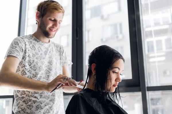 Mulher bonita nova que tem seu cabelo cortado nos cabeleireiros. Jovem cabeleireiro masculino sorrindo e fazendo penteado para o cliente . — Fotografia de Stock