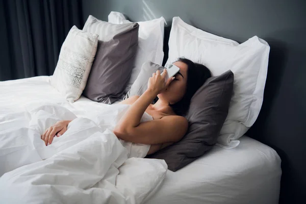 Chica cansada durmiendo en una cama. Duérmete con el móvil en la cara. gesto Facepalm con un teléfono — Foto de Stock