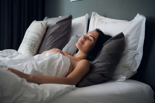 Noche, descanso, comodidad y concepto de personas - mujer joven durmiendo en la cama en casa — Foto de Stock