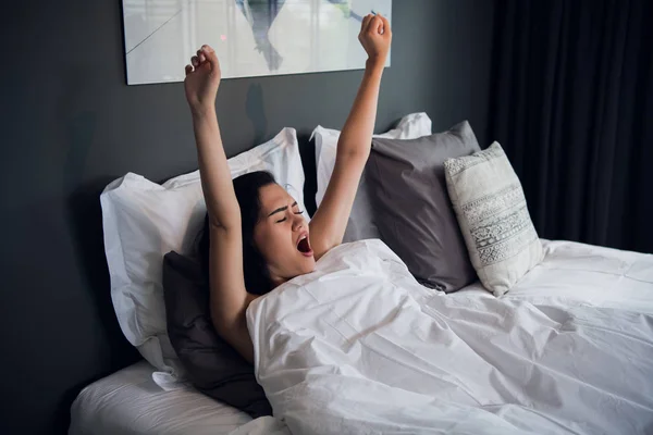 Young pretty woman yawning and stretching in comfortable bed at home. — Stock Photo, Image
