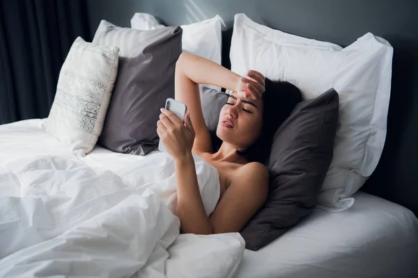 Mujer hermosa enferma acostada en la cama con fiebre alta. Resfriado, gripe, fiebre y migraña con termómetro y teléfono. En el estrés . — Foto de Stock