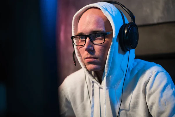 Retrato de un joven concentrado en gafas y auriculares en cuarto oscuro jugando juego de ordenador en línea o compitiendo en un torneo de esport en línea —  Fotos de Stock