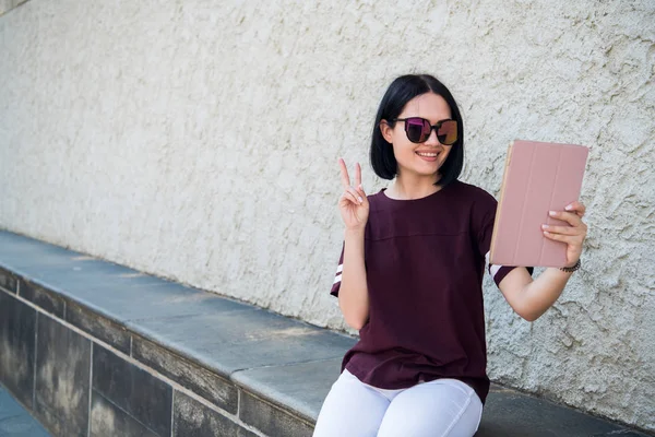 Autorretrato de chica positiva alegre disparando selfie en la cámara frontal con dos manos teniendo videollamada con amigo gestos v-signo al aire libre — Foto de Stock