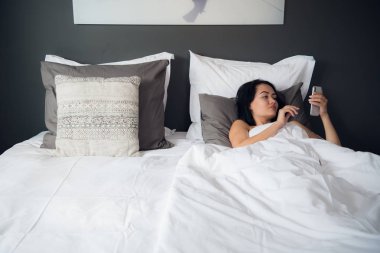 Güzel ve genç birbayan battaniye ile örtülü ile akıllı telefon yatakta yatarken