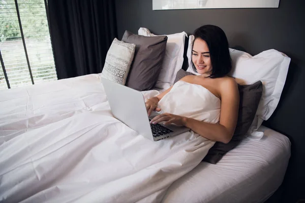 Mujer trabajando en un portátil y tomando café en la cama en casa por la mañana —  Fotos de Stock