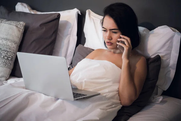 Hermosa mujer acostada en la cama y haciendo una llamada telefónica. Chica joven usando su portátil en casa. Hermosa mujer relajándose en casa . — Foto de Stock