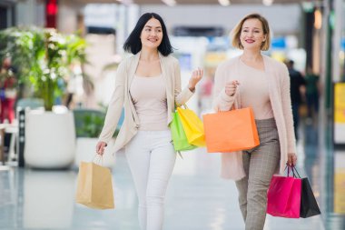 İki mutlu genç kadın alışveriş merkezi alışveriş torbaları ile yürüyüş