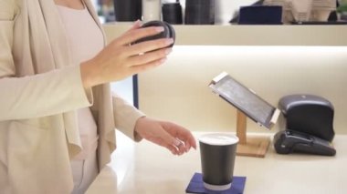 Ağır çekim yakın çekim shot genç bir kadın kahve satın alır ve siyah kağıt bardak kahve barda kapakta kapatır