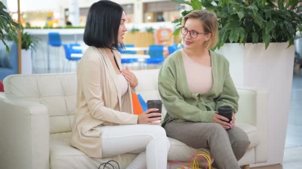 Twee mooie jonge dames rust en iets na het winkelen in het winkelcentrum te bespreken. Afhaalmaaltijden koffie drinken — Stockvideo