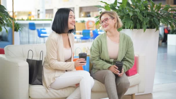 Dvě kamarádky baví v nákupním středisku, mají přestávku, pití kávy a mluví — Stock video