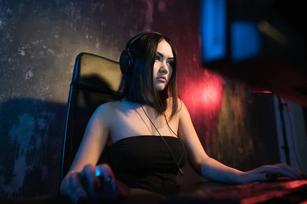 彼女のパーソナルコンピュータ上で一人称シューティングオンラインビデオゲームで遊んで笑顔美しいプロゲーマーの女の子の肖像画ショット。眼鏡をかけ、ヘッドセットに話すカジュアルかわいいギーク — ストック写真