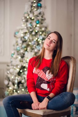 Mutlu genç kadın Noel ağacının yanında oturuyor..