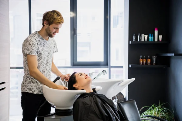 Uomo parrucchiere lavaggio testa cliente. Un padrone di capelli dell'uomo che innaffia i capelli delle ragazze con una doccia in uno studio di capelli . — Foto Stock