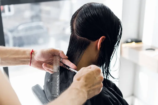 Penata rambut memotong rambut klien di salon dengan gunting penutup. Menggunakan sisir — Stok Foto