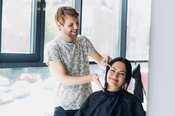 O cabeleireiro faz um corte de cabelo com tesoura de cabelo para uma jovem em um salão de beleza . — Fotografia de Stock