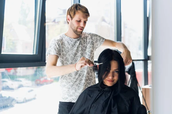 Jovem confiante está olhando para o seu reflexo enquanto penteado cabeleireiro e corte de cabelo clientes — Fotografia de Stock