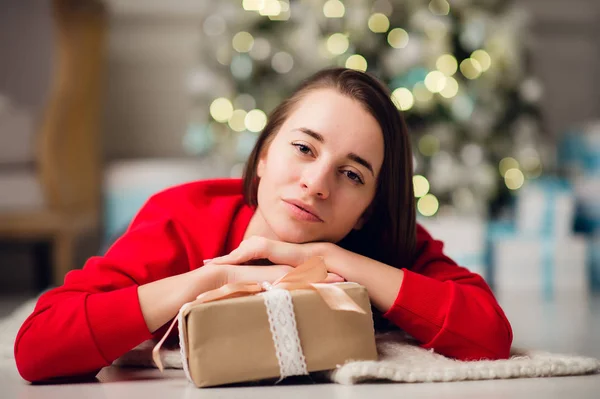 Gyönyörű, boldog fiatal nő fekszik a padlón egy karácsonyi ajándékkal a kezében — Stock Fotó
