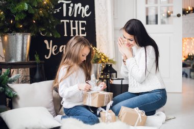 Mutlu Noeller ve mutlu tatiller. Neşeli anne ve tatlı kızı Noel hediyesini açıyorlar. Ebeveynler ve küçük çocuklar Noel ağacının yanında eğleniyorlar.