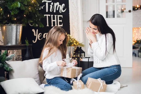 Feliz Navidad y Felices Fiestas. Alegre mamá y su linda hija abriendo un regalo de Navidad. Padre e hijo pequeño divirtiéndose cerca del árbol de Navidad en el interior — Foto de Stock