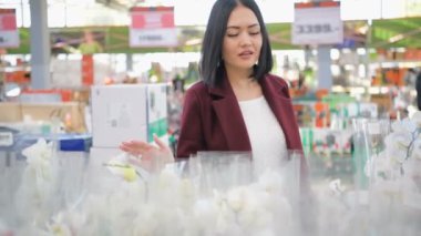 Sunlit Garden Shop 'tan çiçek alan kadın. 4 bin. Çiçekli sera pazarında dekoratif bitkiler için alışveriş yapan genç bir kadın. Ev ve Bahçe kavramı.