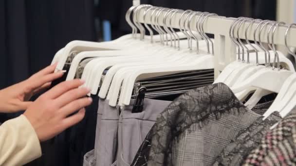 Il primo piano di mani femminili ha strappato una gruccia con vestiti. Le mani delle donne corrono attraverso una rastrelliera di vestiti. Colpo al rallentatore da un lato. Womans mano lisciatura vestiti . — Video Stock