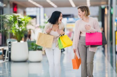 İki mutlu genç kadın alışveriş merkezi alışveriş torbaları ile yürüyüş