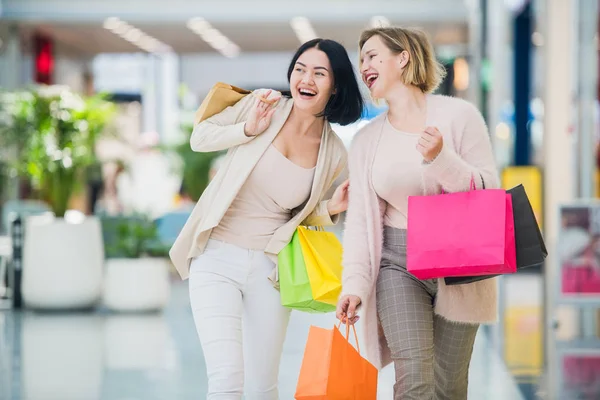 Laughing girls carrying bags with purchases in shopping mall