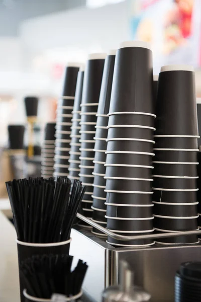 Tazas de papel negro en un mostrador contra el fondo de una barra de café borrosa en el centro comercial con café para llevar para llevar . —  Fotos de Stock