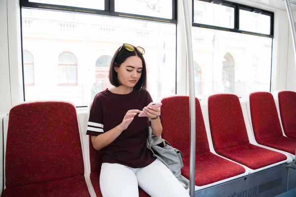Atractiva turista morena viajando en autobús usando la aplicación para navegar en la ciudad, encantadora chica hipster buscando información para el tráfico en la ciudad a través de un teléfono inteligente . — Foto de Stock