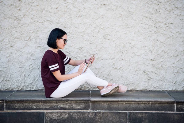 Chica estudiante feliz con sonrisa encantadora leer noticias positivas o navegar por la fuente de noticias a través de las redes sociales utilizando tableta PC, teniendo un pequeño descanso mientras hace la tarea, sentado en la calle . — Foto de Stock