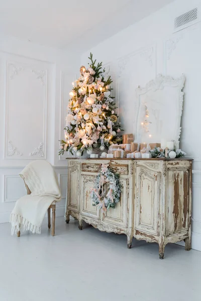 Árbol de Navidad en la cómoda cómoda de madera en el interior blanco, decorado con flores artificiales, guirnaldas y juguetes —  Fotos de Stock