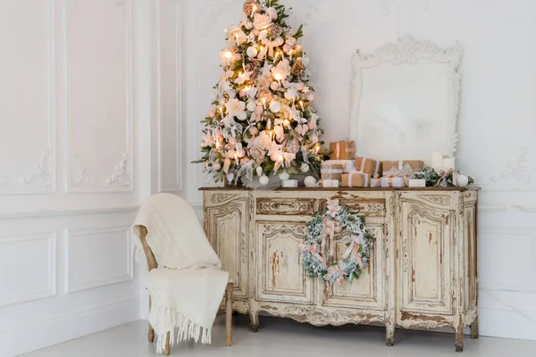 Árbol de Navidad en la cómoda cómoda de madera en el interior blanco, decorado con flores artificiales, guirnaldas y juguetes — Foto de Stock