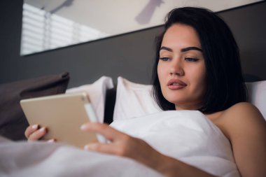 Dijital tablet boş ekran ile tutarak ve yatak odasında gülümseyen çekici esmer kız