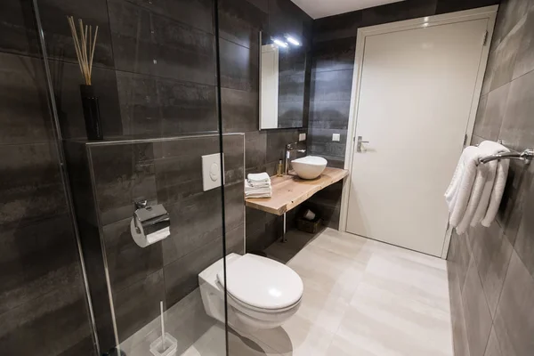 Modern bathroom with a shower area and bath tub including a wall mirror beside a fancy plant near a tap and sink over the wooden counter and dark cupboard. — Stock Photo, Image