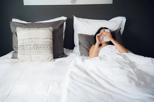 Hermosa joven leyendo mensaje de texto en su teléfono móvil y sonriendo . — Foto de Stock