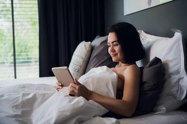 Mujer relajándose en la cama usando tableta digital para videollamada — Foto de Stock