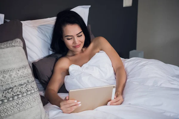 Feliz saludo mujer joven en una videollamada tableta en línea sentado en la cama en el dormitorio en casa — Foto de Stock
