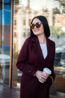 Tek kullanımlık Kupası kentsel arka planda tutan Kış moda neşeli güzel esmer