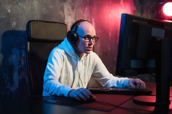 Retrato de un joven concentrado en gafas y auriculares en cuarto oscuro jugando juego de ordenador en línea o compitiendo en un torneo de esport en línea —  Fotos de Stock