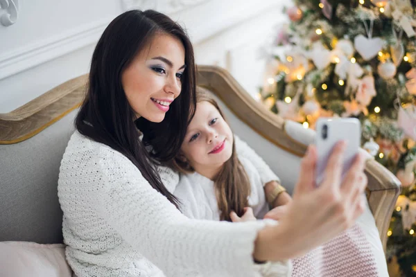 Feliz madre e hija de moda con un pequeño árbol de Navidad y caja de regalo tomando selfie —  Fotos de Stock