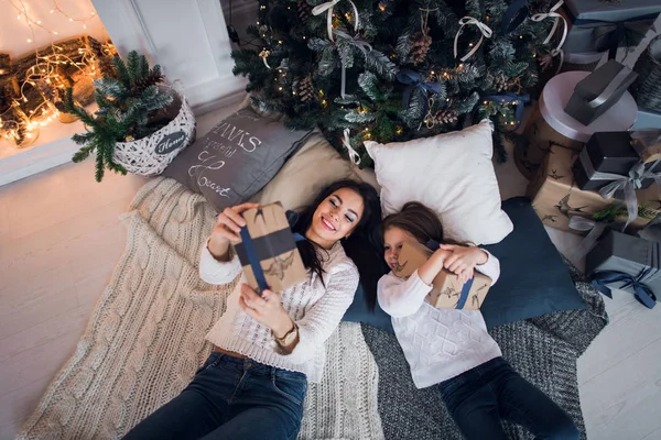 Glückliche Mutter und Tochter beim Öffnen der Weihnachtsgeschenke. Zu Hause versammelte sich die Familie um einen Baum. Weihnachtsbaum mit Geschenken darunter. dekoriertes Wohnzimmer — Stockfoto