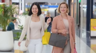 Ağır çekim. Alışveriş, alışveriş merkezinde yürüyen ve Vitrin camekanlar arayan iki güzel kadın. Büyük mağazasında kapalı gülen kızlar.