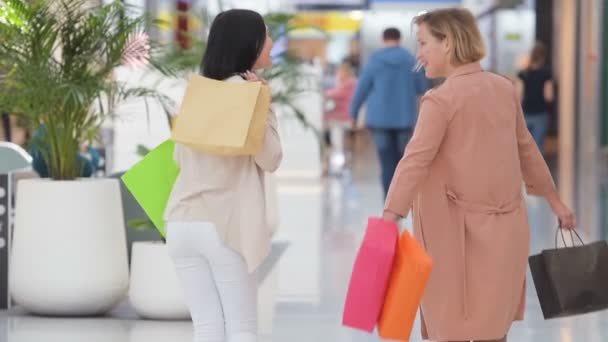 Movimento lento. Rindo meninas carregando sacos com compras no shopping — Vídeo de Stock