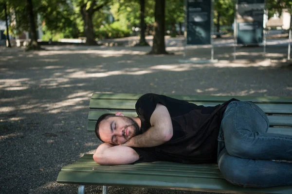 Молодой красивый бородатый мужчина спит на скамейке в парке — стоковое фото