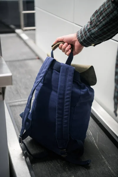 Mans Hand mit einem Rucksack auf dem Gepäckband am Check-in-Schalter im Flughafen. Blauer Rücken am Check-in-Schalter am Flughafen, der das Gewicht misst. Der Flughafenmitarbeiter registriert das Gepäck. — Stockfoto